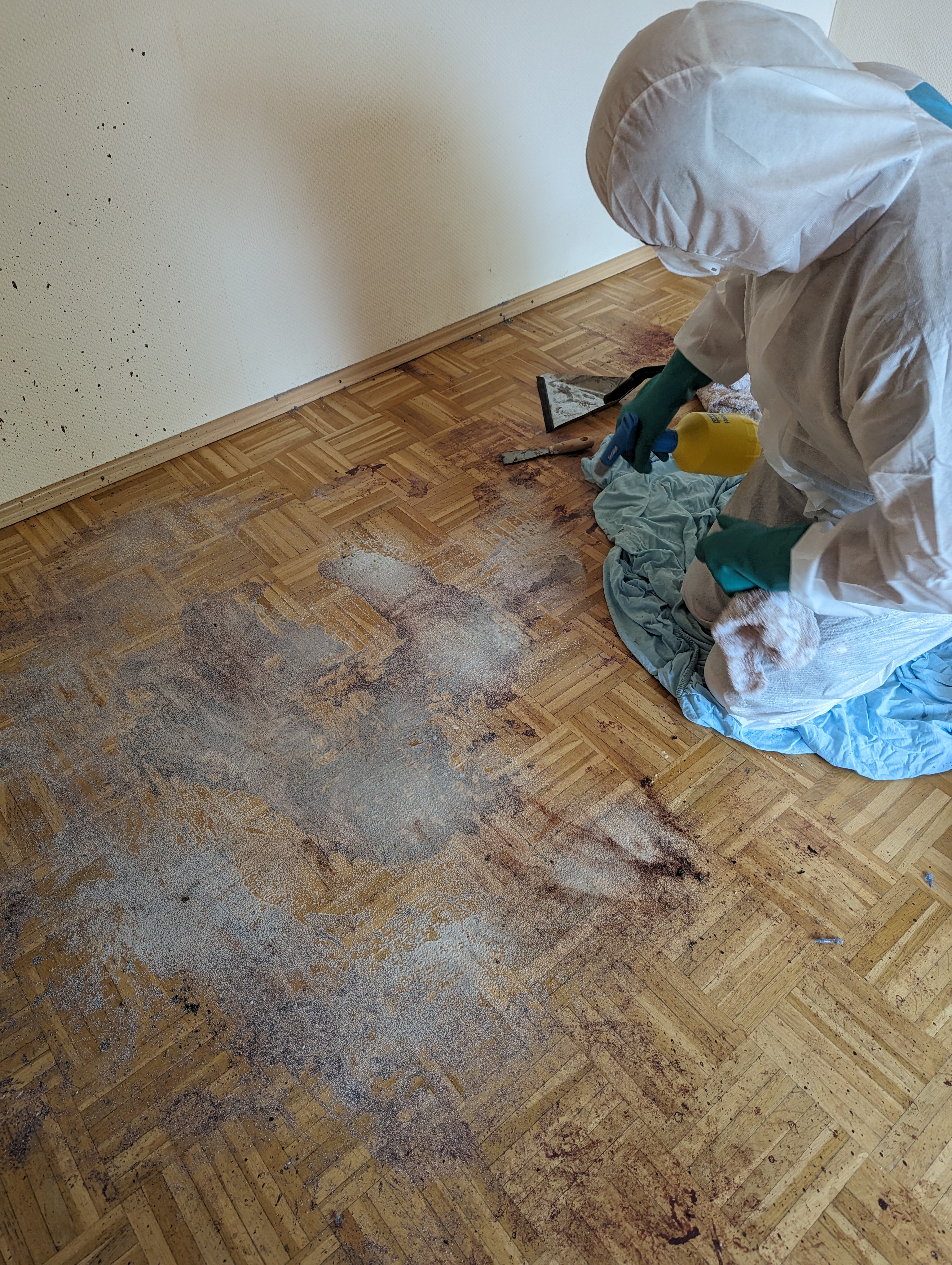 Cleanup worker in protective clothing treating an exposed floor inside a room